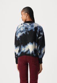 Gestructureerde gebreide trui met een tie-dye patroon in zwart, blauw en crème. Het ontwerp heeft een relaxte pasvorm en geribbelde manchetten, gecombineerd met bordeauxrode broek.