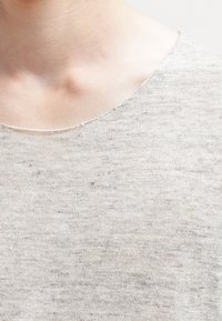 Maglione grigio chiaro lavorato a maglia con scollatura rotonda. Il tessuto appare morbido con un motivo leggermente testurizzato e sottili variazioni di colore.