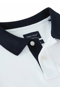 Polo blanc avec un col marine, doté d'une patte de boutonnage à deux boutons, d'un tissu texturé et d'une étiquette portant la mention "Eden Park" au niveau du cou.