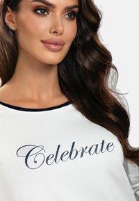 Camicia di cotone bianca con colletto blu navy, caratterizzata dal testo "Celebrate" in un font glitterato blu navy, mostrata su uno sfondo chiaro e liscio.