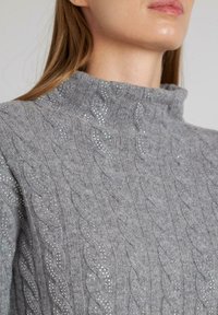 Maglione grigio a maglia con collo alto, con accenti di strass intrecciati che aggiungono texture e dettagli.