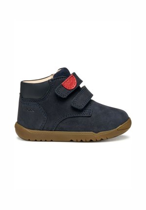 Donker marineblauw suede enkelboot met dubbele klittenbandsluitingen, bruine rubberen zool en rode accenten op de banden. Beschikt over gladde leren details.