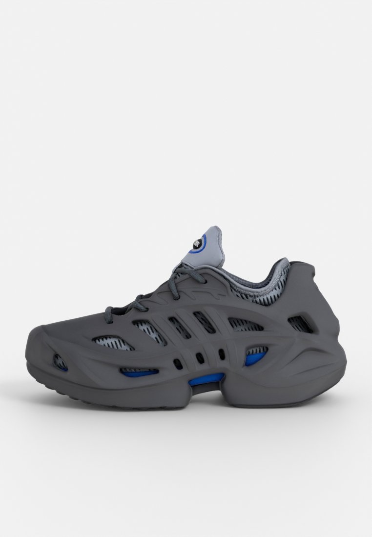 Zapatilla deportiva gris con paneles de malla, líneas curvadas y una suela gruesa. Presenta acentos azules y un cuello texturizado para mayor comodidad y transpirabilidad.