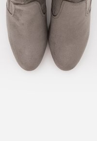Botines de ante gris con una textura suave, punta redondeada y un sutil diseño de costura en los laterales. Tacón plano, estilo minimalista.