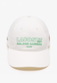 Gorra de béisbol blanca de algodón con texto bordado en verde "LACOSTE ROLAND GARROS CLUB" en la parte frontal y un pequeño logo en el lateral.