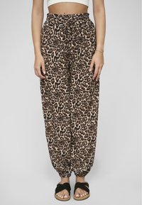 Leopardenmuster-Hosen aus leichtem Material mit einem elastischen Bund und gerafften Bündchen, ergänzt durch schwarze Slidesandalen.