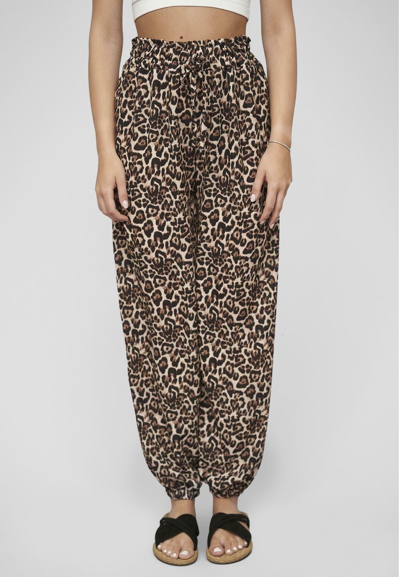 Leopardenmuster-Hosen aus leichtem Material mit einem elastischen Bund und gerafften Bündchen, ergänzt durch schwarze Slidesandalen.