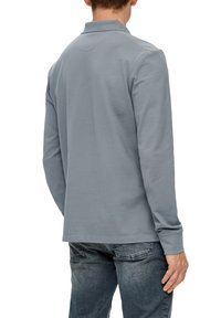 Graues Langarm-Polohemd mit Kragen, das eine glatte Textur und eine lockere Passform aufweist, kombiniert mit blauen Denim-Jeans.