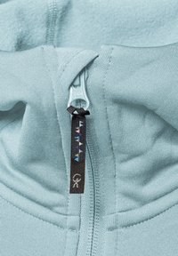 Ljusblå hoodie med YKK-dragkedja, prydd med en svart dragkappa dekorerad med färgglada triangulära mönster och en logotags. Mjuk textur.