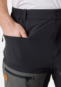 Schwarze Outdoor-Hosen mit dehnbarem Bund, Reißverschlusstaschen und kontrastierendem grauem Stoff am unteren Bein. Strukturiertem Stoff mit Logodetail.