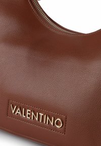 Braune Lederhandtasche mit goldenem Reißverschluss und erhabenem, goldenem Valentino-Schriftzug auf einem aufgenähten Lederetikett.