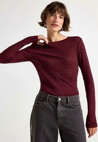 Bordeauxrode en zwarte gestreepte top met lange mouwen en een boothals. Zachte stof, aansluitende pasvorm, gecombineerd met hooggetailleerde donkergrijze broek.