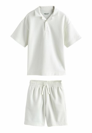 Biała koszulka polo z krótkim rękawem z guzikami oraz szorty z elastycznym pasem i sznurkiem, oba wykonane z lekkiego materiału.