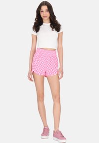 Shorts a quadri rosa con una cintura elastica, abbinati a un crop top bianco aderente e sneaker rosa chiaro. Tessuto morbido e vestibilità comoda.