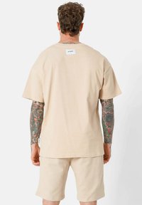 Beige T-shirt met korte mouwen en een relaxte fit, voorzien van een label op de achterkant, gecombineerd met bijpassende beige shorts. Soepele stof textuur.