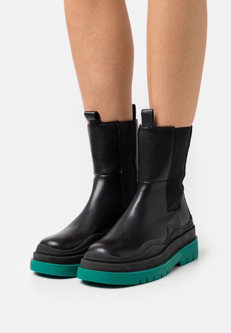 Stivali alla caviglia in pelle nera con upper testurizzato, pannelli laterali elasticizzati e suola chunky teal con modelli di battistrada pronunciati.