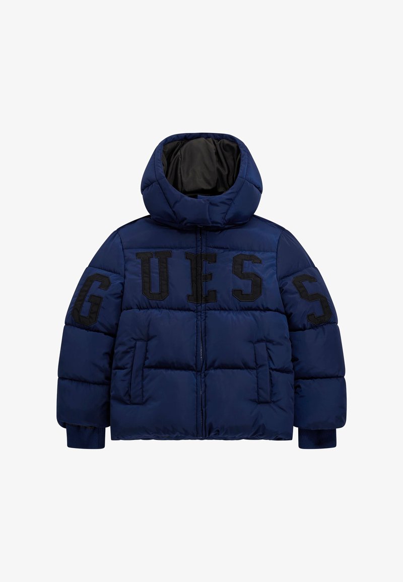 Temno modra puhovka z visokim ovratnikom in kapuco, z velikimi črnimi črkami "GUESS" spredaj ter rebrastimi manšetami. Gladka tekstura z quiltanim vzorcem.