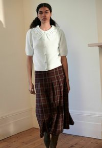 Lysblå ribbet cardigan med runde knapper og en blonde-krave, parret med en brunternet midi-nederdel med plisseringer.