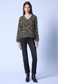 Svart blommönstrad blus med V-hals och långa puffärmar, i kombination med mörka jeans och svarta klackstövlar. Enkel och elegant design.