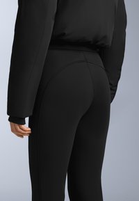 Czarny zestaw aktywny składający się z puchowej kurtki i legginsów z wysokim stanem. Legginsy mają gładką teksturę i subtelne przeszycia.