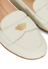 Weiße Leder-Loafer mit strukturiertem Finish, runder Spitze, Stickdetails und einem goldfarbenen Logoplatte-Element auf der Vorderseite.
