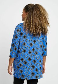 Niebieska tunika z geometrycznym wzorem w kolorach czarnym i niebieskim, z rękawami do łokcia i luźnym krojem. Miękka tkanina i swobodny fason.