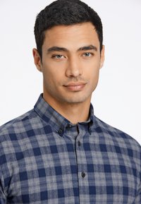 Camisa de cuadros azul y gris con cuello abotonado, hecha de una tela de textura suave, con botones negros y un corte clásico.