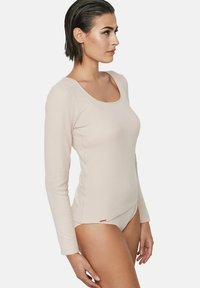 Haut à manches longues de couleur beige clair en tissu doux, avec un col dégagé, une silhouette ajustée et des détails cousus le long des coutures.