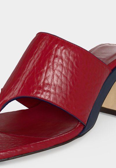 Κόκκινο δερμάτινο mule με ανοιχτή μύτη και φαρδιά λουριά, άκρες σόλας σε ναυτικό μπλε και τακούνι block με λεπτομέρειες σε μπεζ και ναυτικό μπλε χρώμα.