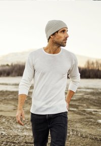 Hvid langærmet skjorte med rund halsudskæring, kombineret med en grå hue og mørke jeans. Blødt stof med ribbestrik i ærmerne.