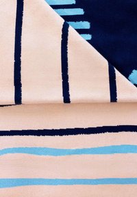 Tekstylia z beżowym tłem i granatowymi oraz jasnoniebieskimi pasami. Wzór zawiera nieregularne kształty o zróżnicowanej szerokości i fakturze.