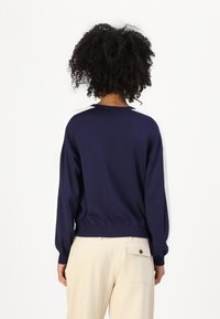 Pullover blu scuro con una vestibilità rilassata, polsini e orlo a coste. Texture liscia, spalle scese e design minimalista.