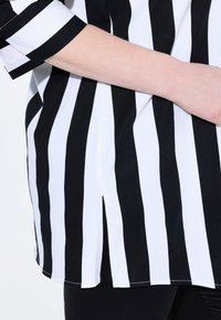 Svart-och-vitt randig topp med lös passform, med korta ärmar och en sidosprund. Tyget verkar slätt med en lätt lyster.
