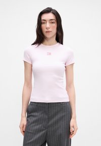 Heled roosa ribaga lühikeste varrukatega T-särk, mille keskel on väike logo. Kombineeritud hallide triibuliste pükstega, esitatuna neutraalses taustas.