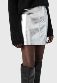 Sudraba metāliska mini svārki ar gludu faktūru, kombinēti ar melnu pūkainu džemperi. Raksturīga taisna piegriezuma dizains un redzamas šuves.