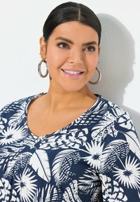 Námořnická modrá tričko s bílými květinovými a listovými vzory, v-výstřih, krátké rukávy a měkká, strukturovaná látka.