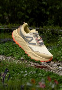 Chaussure de randonnée jaune clair avec une tige à motifs, des accents gris et une semelle extérieure orange vif. Comprend une semelle rembourrée et une surface texturée.