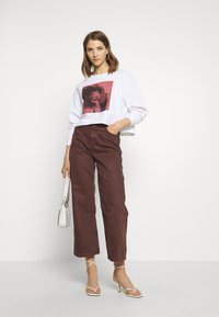 Sweatshirt branco com estampado gráfico, combinado com calças largas burgundy e sandálias brancas de tiras. Acessorizado com uma pequena mala branca.