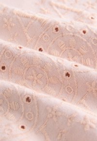 Jemná ružová látka s vyšívanými kvetinovými vzormi. Textúrovaný povrch obsahuje malé dierky a vystúpené stehy.