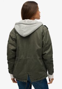 Olivengrøn, let jakke med grå hætte, elastisk snøre i kanten og ribstrikkede ærmegab. Har en åbning bagpå og sidelommer.