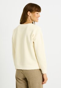 Sudadera color crema con cuello redondo, puños y dobladillo acanalados. Confeccionada en tejido suave, presenta un corte relajado y un diseño minimalista.