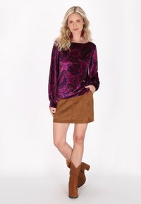 Lila Paisley-musterter Samtoberteil mit langen Ärmeln und Rundhalsausschnitt, kombiniert mit einem braunen Wildleder-Minirock und braunen Stiefeletten.