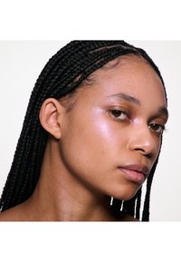 Portrait d'une personne avec des cheveux tressés foncés et un teint lisse, mis en valeur par un subtil éclat. Ses traits comprennent des yeux marron et des lèvres naturelles.