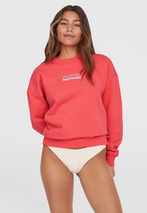 Sweatshirt corail avec un col ras du cou et une coupe décontractée, arborant le texte blanc "The Future Surf Society". Porté avec un bas de bikini de couleur claire.