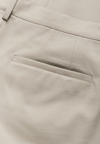 Pantalons beiges avec une texture de tissu lisse, dotés d'une poche arrière simple et de détails de couture soignés.