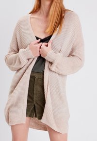 Ljusbeige öppen stickad cardigan med en mjuk textur, som har en avslappnad passform, långa ärmar och ribbade detaljer.