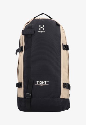 Sac à dos avec une combinaison de couleurs noire et beige, en tissu durable, et avec des boucles latérales. Présente le logo de la marque et le texte "TIGHT™ LARGE" à l'avant.
