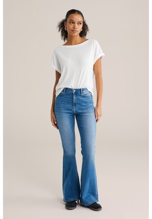 Biała bluzka z krótkim rękawem z teksturowanym wzorem w zygzaki, w połączeniu z jasnoniebieskimi spodniami dzwonami. Uzupełnieniem stroju są czarne buty.