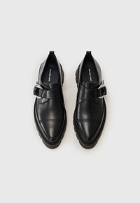 Black leather shoes with a rounded toe, flat sole, and an adjustable strap featuring a silver circular buckle. Smooth texture, no patterns.