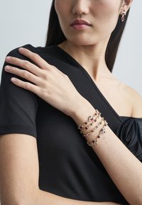 Gold-tone multi-strand bracelet with red and purple stones, worn on a black top. Smooth texture and delicate accents are prominent.